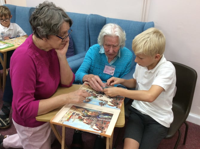 A pupil from St Lawrence CE Primary School in Alton does a jigsaw puzzle with two visitors to The Dementia Café in Alton Community Centre, November 2022.