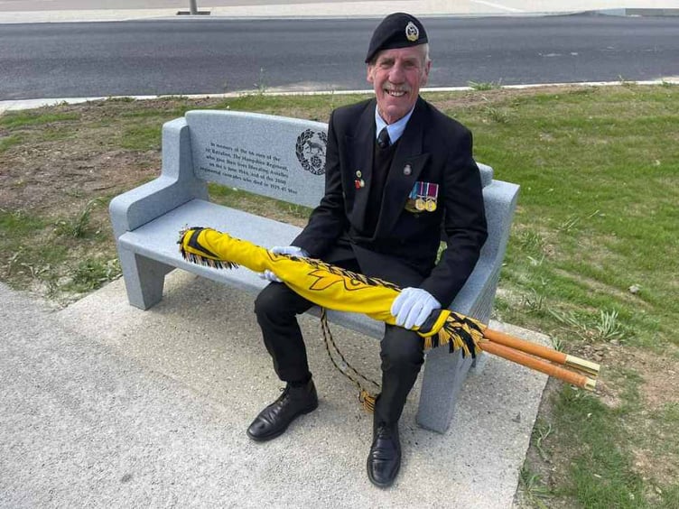 Bob Graham, with the Royal Hampshire Regimental Standard, tries out the granite bench presented to the village of Asnelles in France, May 2023.
