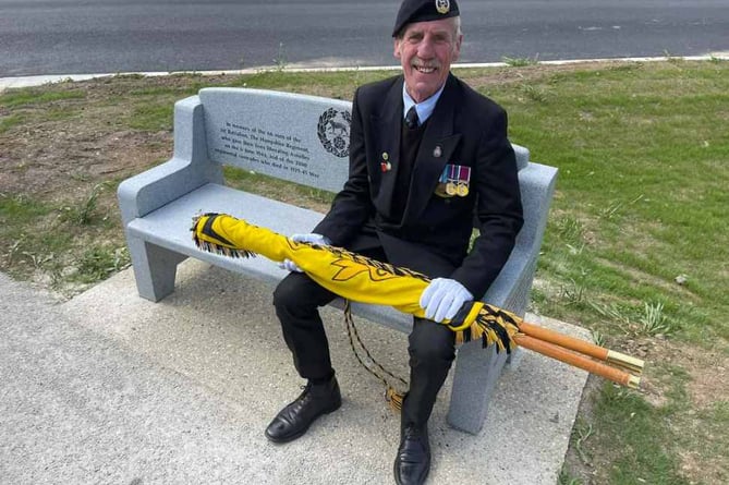Bob Graham, with the Royal Hampshire Regimental Standard, tries out the granite bench presented to the village of Asnelles in France, May 2023.