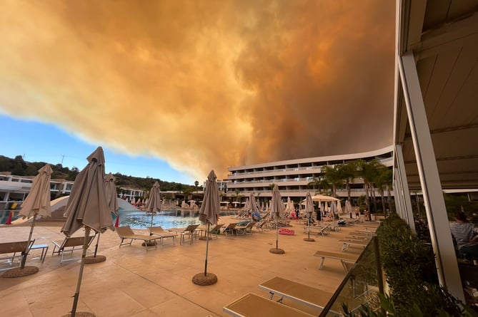 Smoke from the wildfires on Rhodes loom over the hotel. Guests had to literally run for their lives after being ordered out by the Greek army.